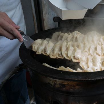 A person cooking dumplings on a large pan with steam rising.