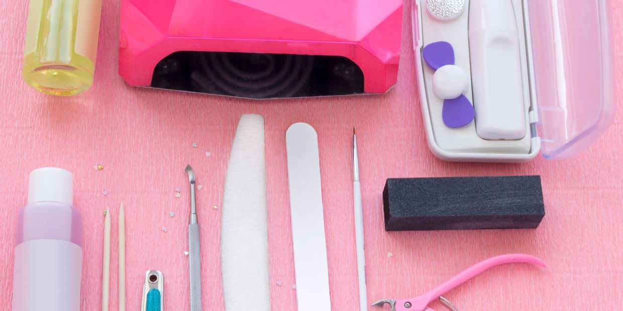 A complete nail care kit with tools and pink LED lamp on a pink surface.