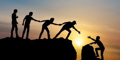 People helping each other climb rocks at sunset.