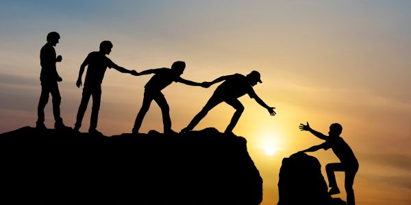 People helping each other climb a cliff at sunset.