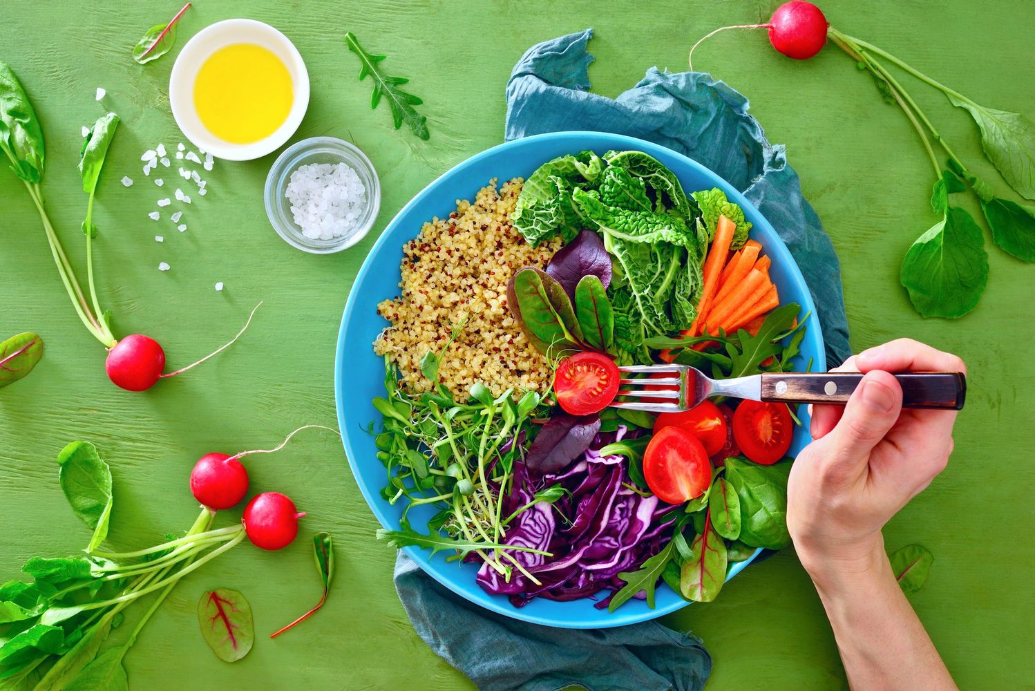 Colorful healthy salad with quinoa, vegetables, and a hand holding a fork.