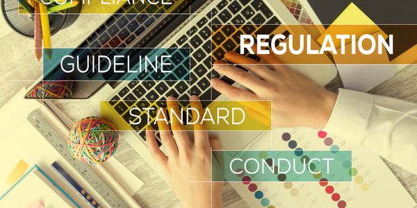 Hands typing on laptop with compliance and regulation keywords overlay.