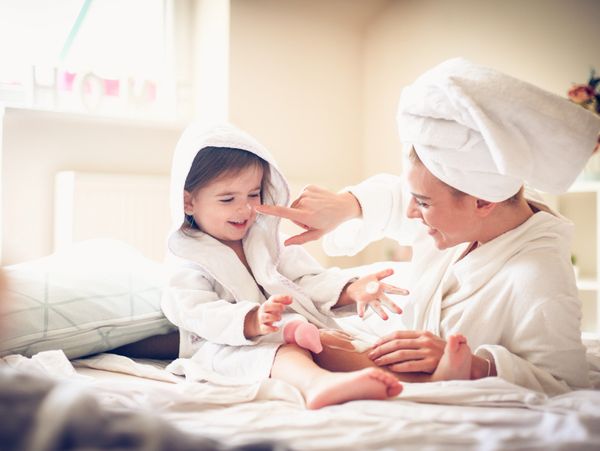 Mother and child in bathrobes playfully touching noses on a bed.