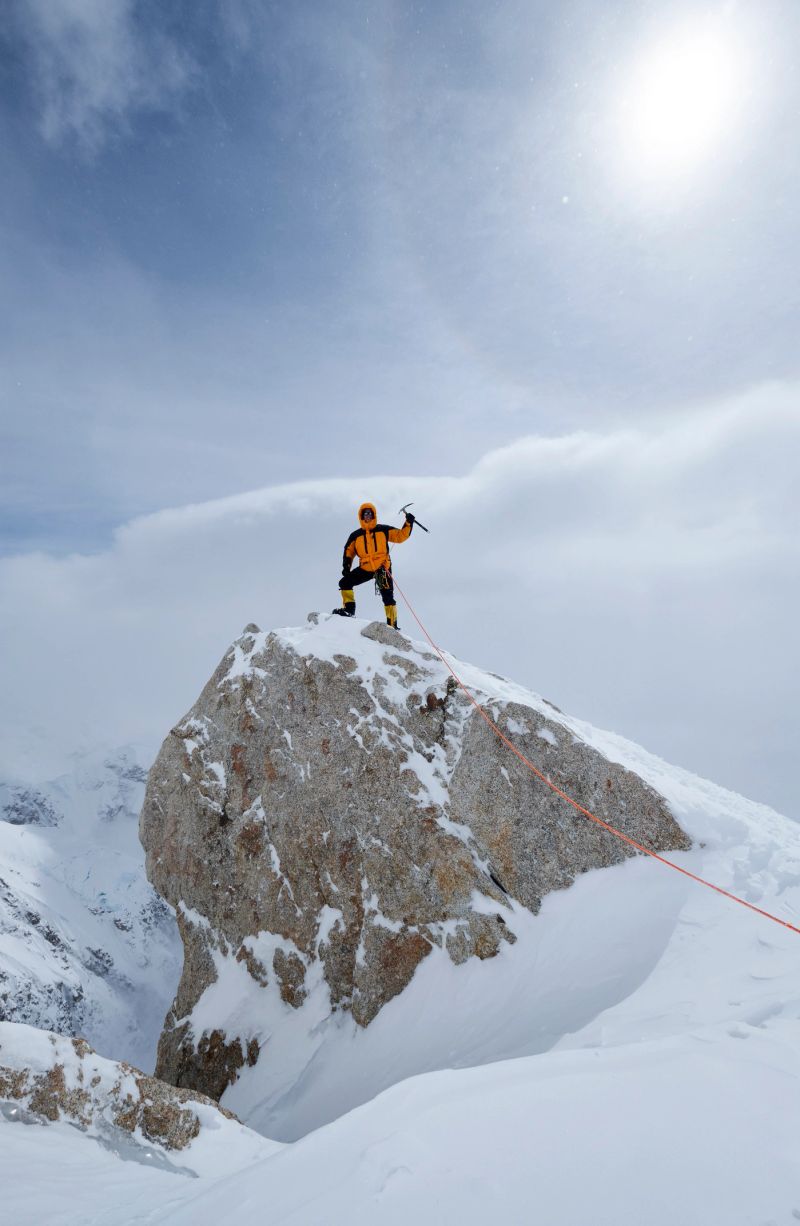Mountaineer poses on the rock at the edge of the world, on Denali, on a rope with ice ax in his hand