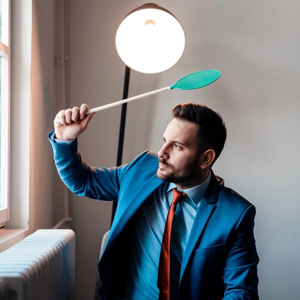 Man in a blue suit holding a fly swatter near a window.