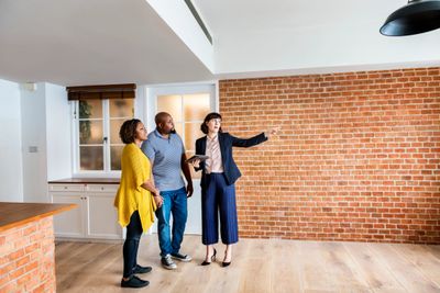 Real estate agent showing a couple a new home with exposed brick walls.