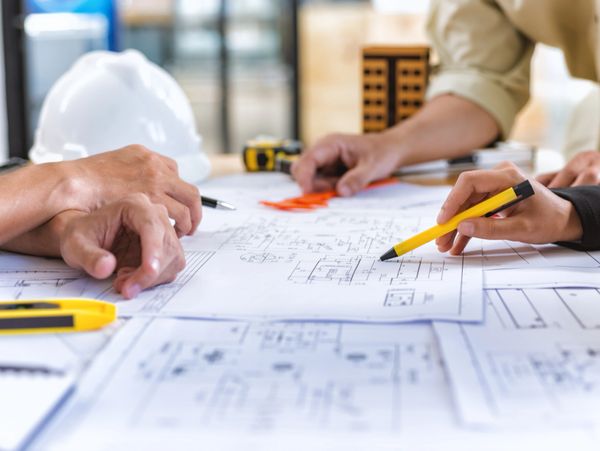 People discussing architectural blueprints with tools on a table.