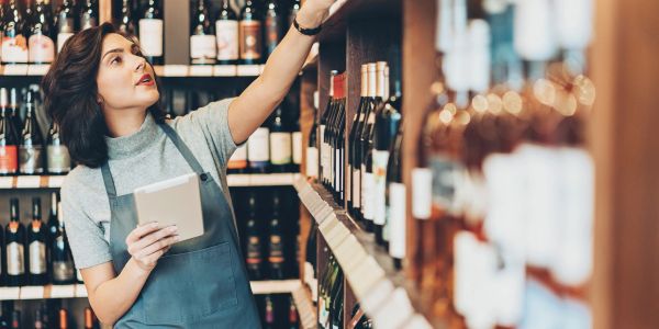 A woman in an apron organizing wine bottles on a shelf.