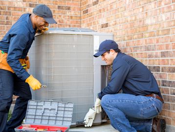 Two HVAC technicians inspecting an outdoor air conditioning unit.