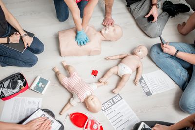 CPR training class with adult and infant mannequins, first aid supplies.
