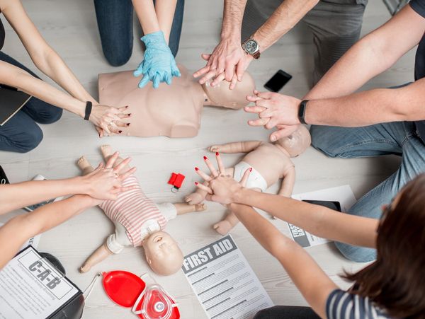 Group practicing CPR on adult and infant mannequins during a first aid training session.