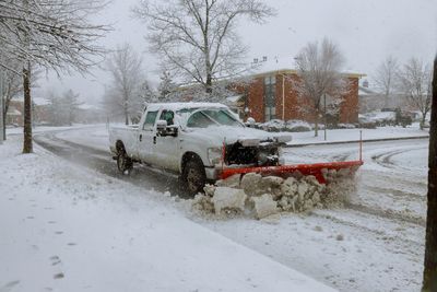 A white pickup truck plowing snow on a snowy street in a residential area.