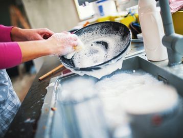 Person washing a soapy frying pan in a kitchen sink.