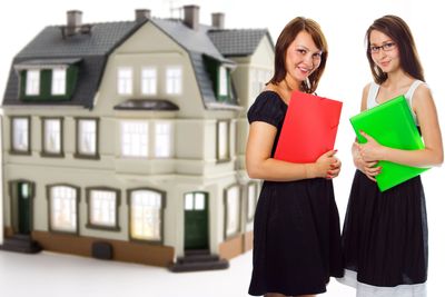Two women holding folders standing in front of a model house.