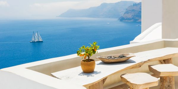 Scenic seaside view with sailboat and white terrace seating.