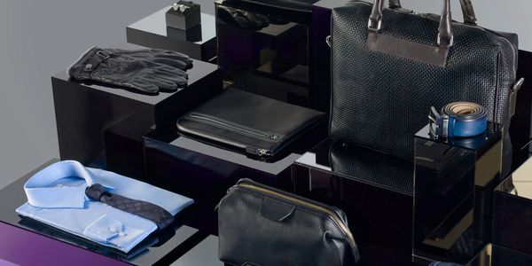 Elegant men's accessories including gloves, bags, belt, shirt, and tie arranged on black surfaces.
