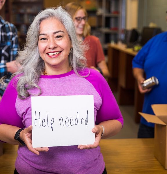 Woman smiling holding a sign that says help needed.