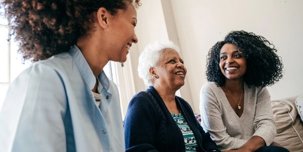Three women of different generations smiling and engaging in conversation indoors.