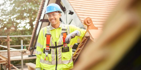 Smiling construction worker in safety gear on a roof.