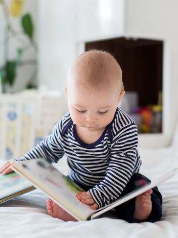 Baby reading a book on bed.