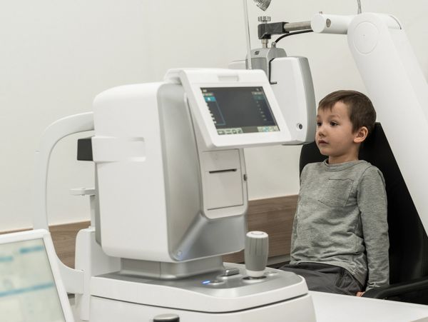 A young boy sits for an eye exam with advanced ophthalmic equipment.