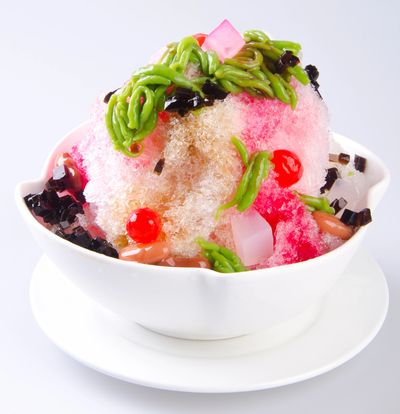 Colorful shaved ice dessert with various toppings in a white bowl.