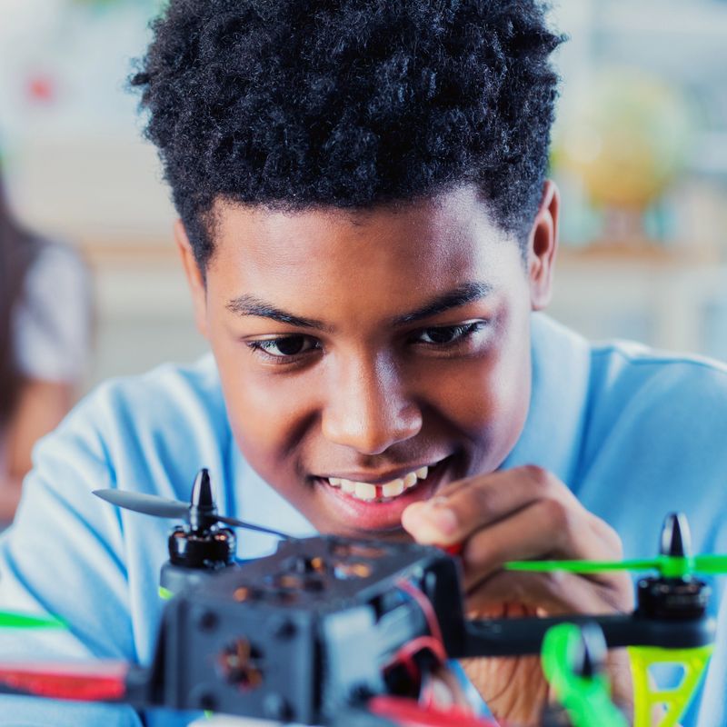 Excited male high school student smiles while assembling a drone during engineering class.