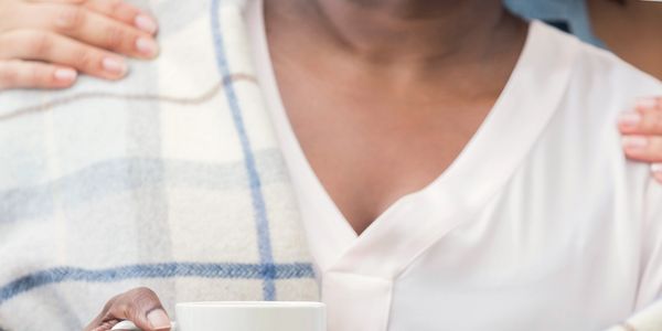 A person holding a cup with hands on their shoulders in a comforting gesture.