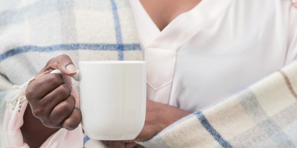 Person wrapped in a cozy blanket holding a white mug.
