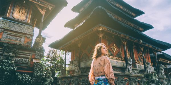 A woman in traditional attire stands by an intricately decorated temple.