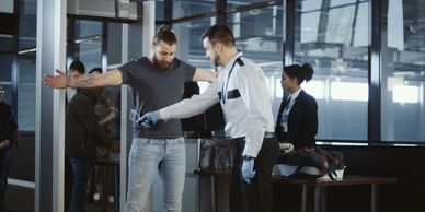 Airport security officer scanning a passenger with a handheld detector.
