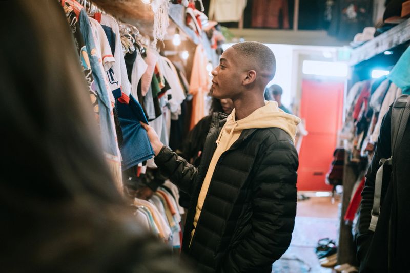 A smiling group of young adults have fun shopping for retro and vintage clothing styles at a second hand thrift store.  Mixed ethnic group.  Horizontal image with copy space.