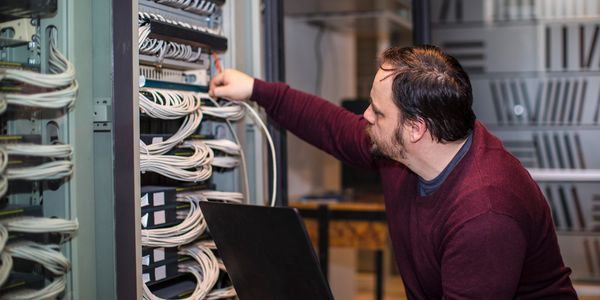 Technician managing cables in a server rack with a laptop.