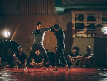 Two men sparring in a gym while others watch.