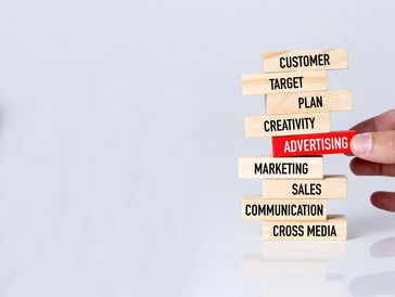 Wooden blocks with marketing and advertising terms stacked, with a hand pulling the advertising block.