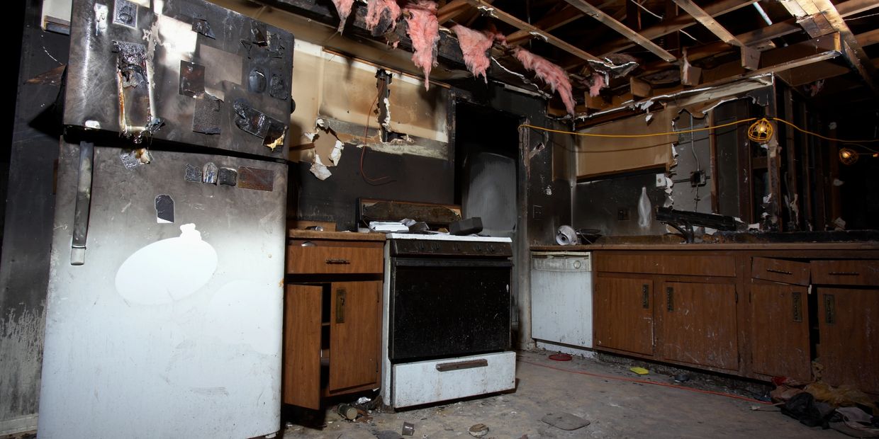 Burnt kitchen with damaged ceiling and appliances.