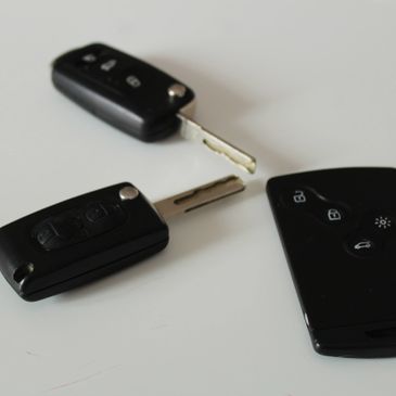 Two car keys and a remote control on a white surface.
