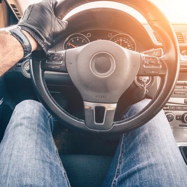 Driver wearing a black glove holding a car steering wheel.