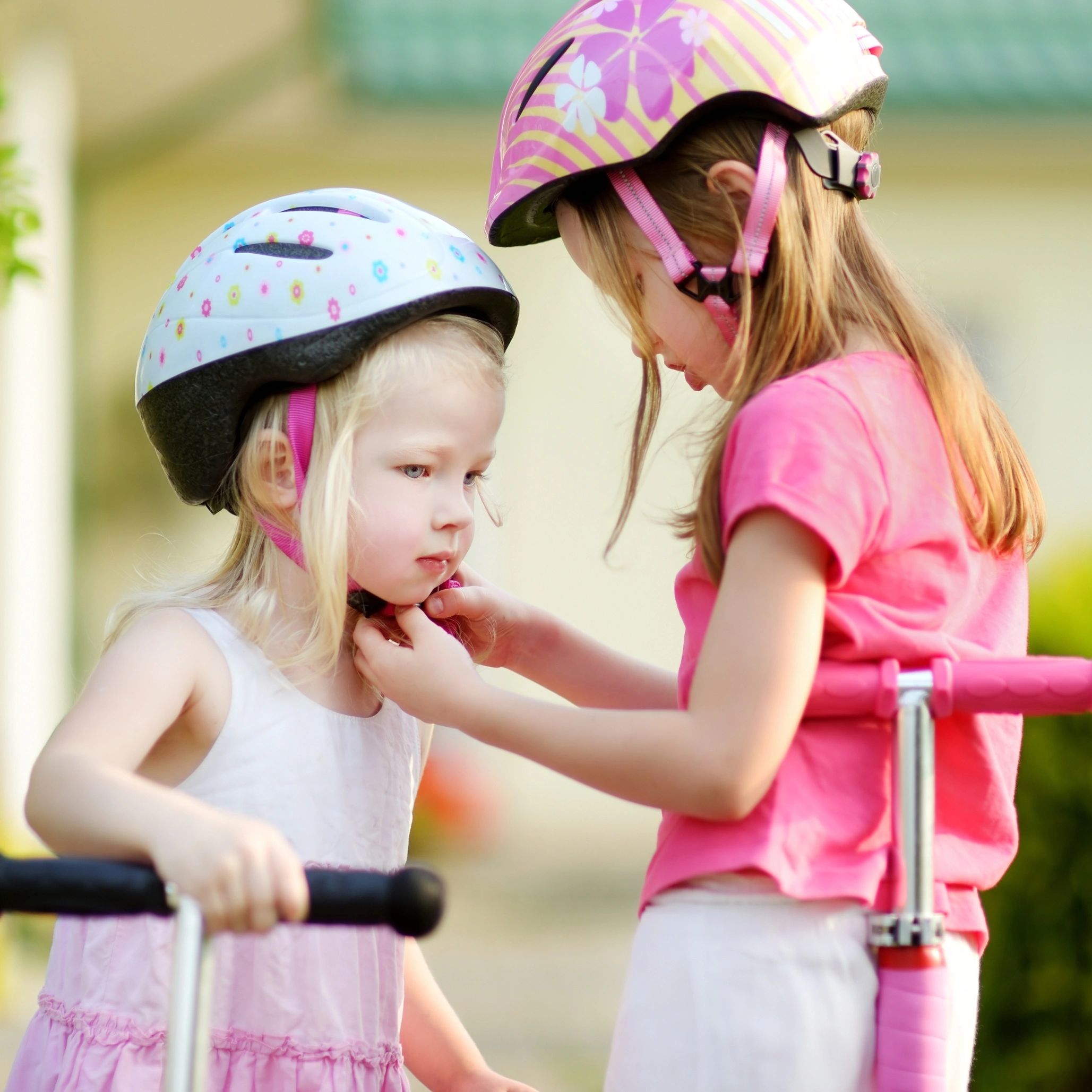 Two girls wearing helmets preparing to ride scooters.