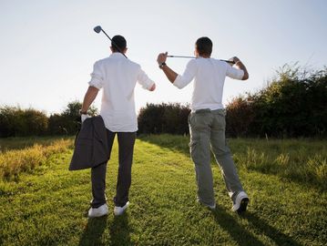 Two men walking on a golf course with clubs and a jacket.