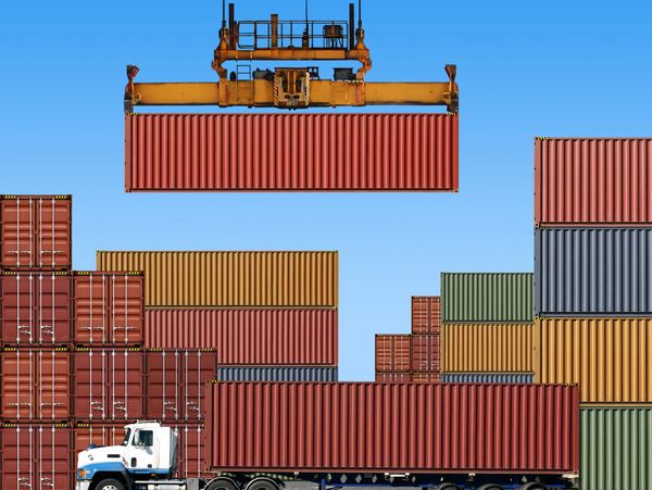 A crane lifting a red shipping container above a truck at a busy container yard.