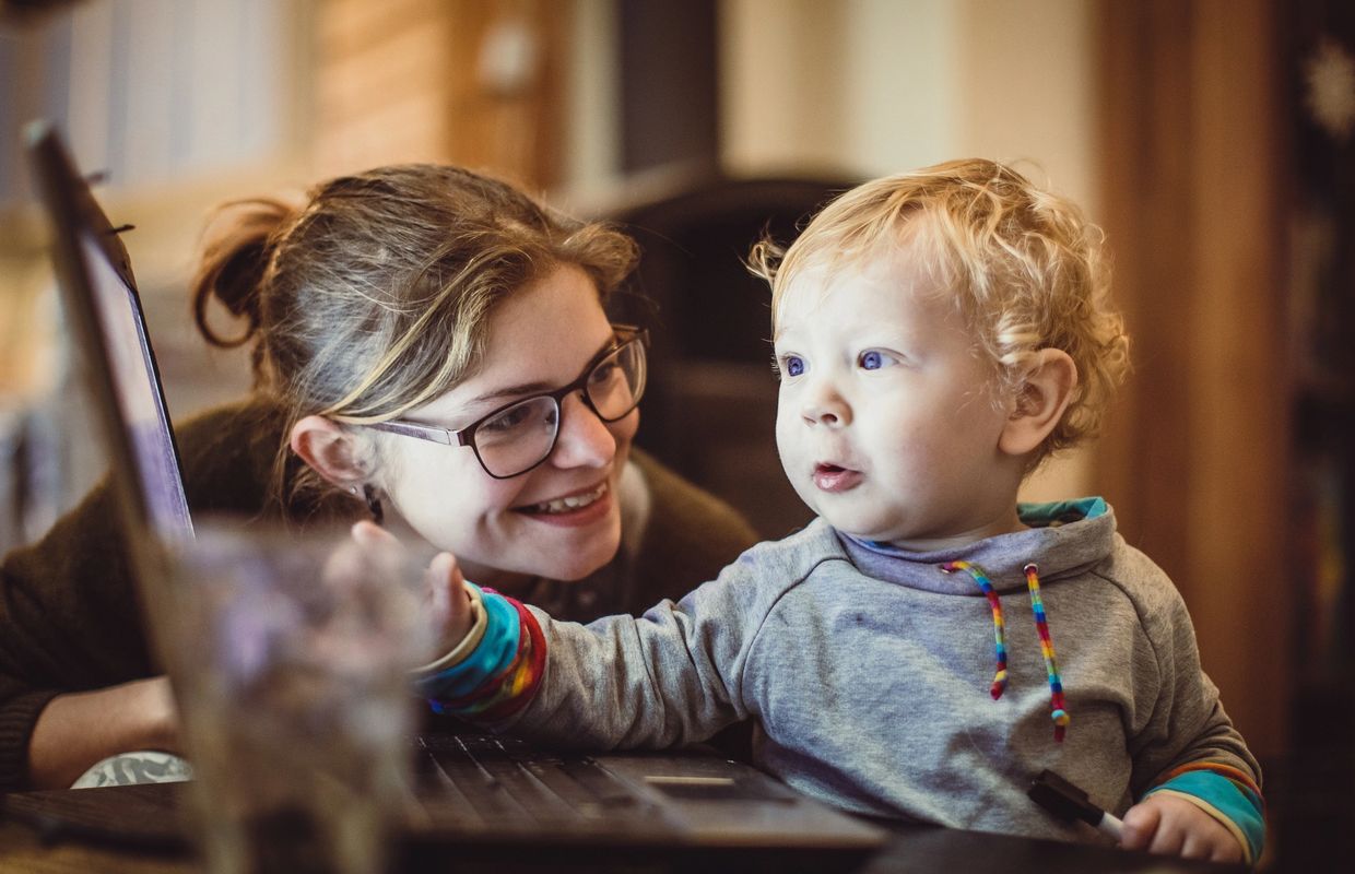 A woman smiles at a toddler using a laptop together.