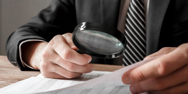 Person examining documents with a magnifying glass.