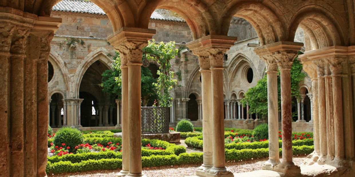 Historic cloister garden with stone arches and greenery.