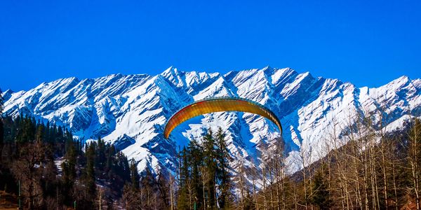 Paraglider soaring against snowy mountain backdrop.