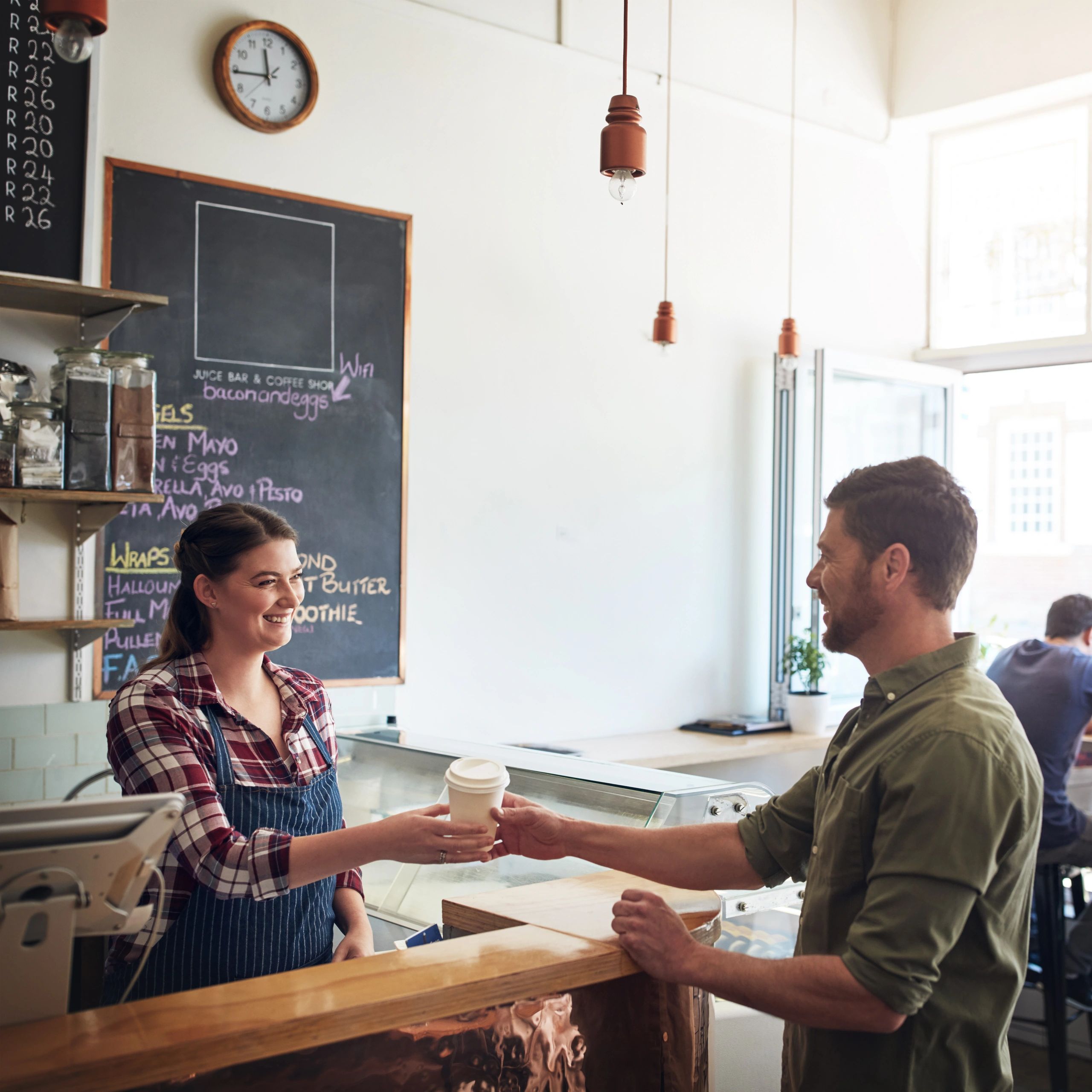 Barista handing a coffee cup to a smiling customer in a cozy café.