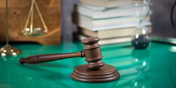 Wooden judge's gavel on table with scales and books.