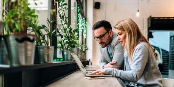 Two people working together on a laptop in a modern office.