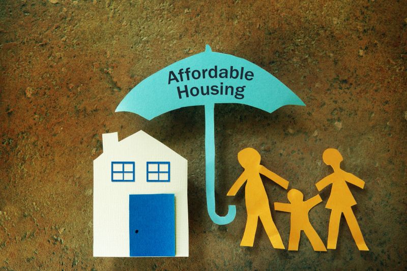 Paper cutout family with house under an Affordable Housing umbrella