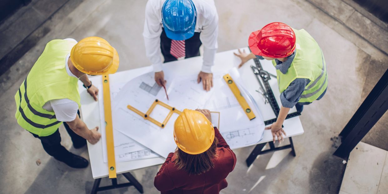 Engineer and supplier team reviewing technical drawings on an industrial production floor.